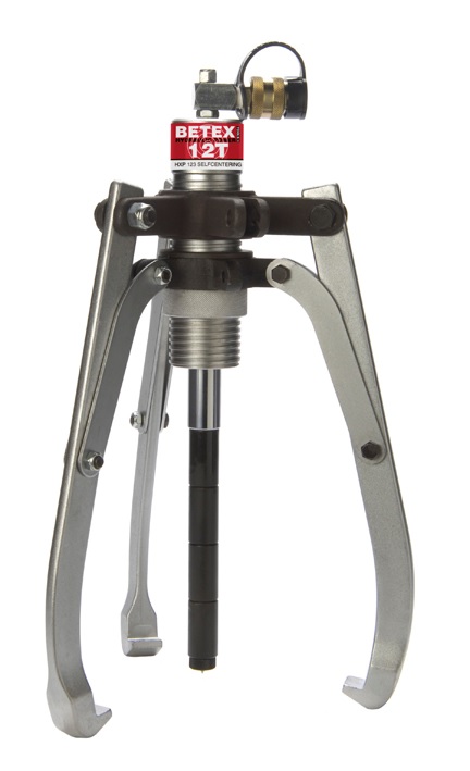 Zdjęcie przedstawia profesjonalny zestaw ściągaczy hydraulicznych BEGA BETEX z serii HXP. Narzędzia te są przeznaczone do najcięższych prac demontażowych w przemyśle.  Charakterystyka sprzętu Kluczową cechą, kt&oacute;ra wyr&oacute;żnia tę serię, jest zastosowanie zewnętrznej pompy hydraulicznej połączonej z cylindrem ściągacza za pomocą elastycznego węża wysokociśnieniowego. Taka konstrukcja zapewnia operatorowi większą swobodę pracy i pozwala na obsługę z bezpiecznej odległości.  Na zdjęciu widać następujące elementy:  Korpus ściągacza o solidnej, masywnej budowie, zazwyczaj w kolorze niebieskim lub czarnym. Na korpusie widoczne jest logo BEGA BETEX oraz oznaczenie modelu HXP.  Trzy ramiona (szczęki), kt&oacute;re można łatwo zamontować i ustawić.  Oddzielna pompa hydrauliczna z manometrem, kt&oacute;ry pozwala na precyzyjną kontrolę siły nacisku. Pompa jest umieszczona obok ściągacza.  Wysokociśnieniowy wąż hydrauliczny, kt&oacute;ry łączy pompę z cylindrem ściągacza.  Zastosowanie i kontekst wizualny Cały zestaw wygląda na kompletny i gotowy do użycia. Narzędzia mogą być ułożone w dedykowanej walizce transportowej, co podkreśla ich przeznaczenie do pracy w terenie, lub na solidnym warsztatowym stole, co sugeruje ich stałe miejsce w hali produkcyjnej. Zdjęcie doskonale oddaje potęgę i precyzję tego narzędzia, zaprojektowanego do szybkiego i bezpiecznego demontażu element&oacute;w maszyn, takich jak łożyska, koła zębate czy koła pasowe, bez ich uszkodzenia.